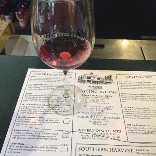 A wine glass sits on a menu featuring various wines and tasting options from Habersham Estate Winery.