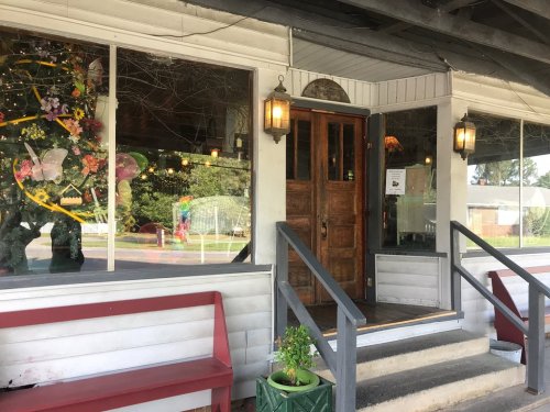 A charming storefront with wooden doors, large windows, and decorative plants, inviting visitors inside.