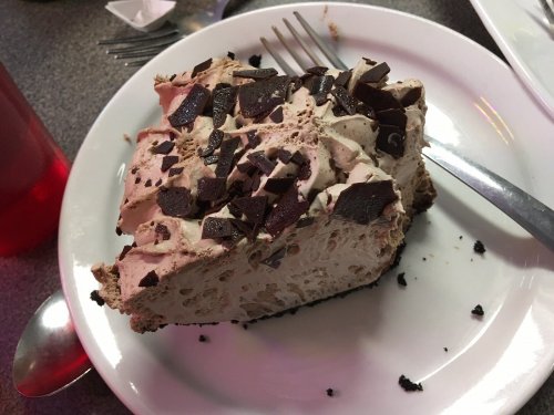 A slice of chocolate mousse cake topped with chocolate shavings on a white plate, with a fork beside it.