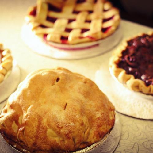 A variety of pies on a table, including a whole pie, a lattice-topped pie, and a chocolate pie.