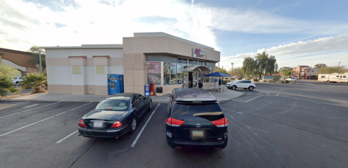 A convenience store with large windows, surrounded by parked cars and a clear blue sky.