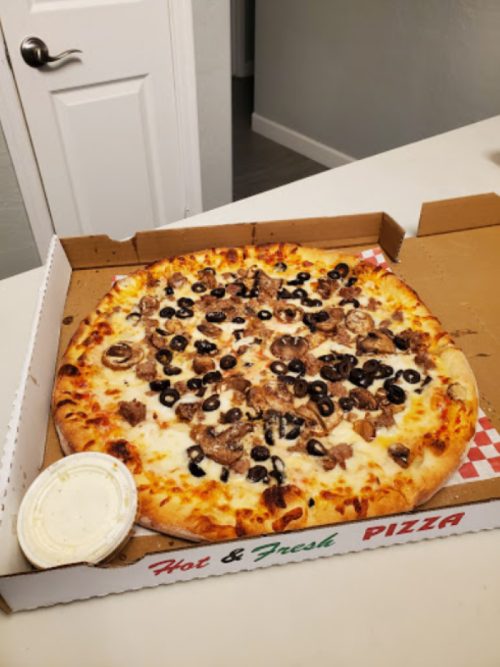 A pizza topped with mushrooms and black olives, placed in an open pizza box with a side of dipping sauce.