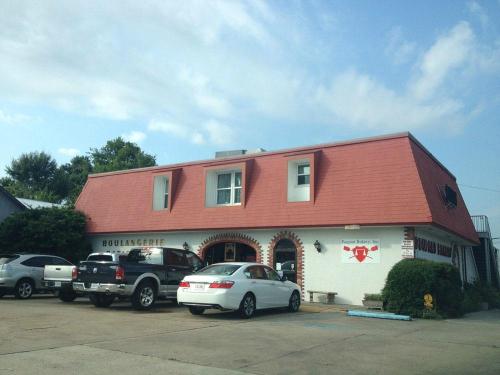 A bakery with a red roof and white exterior, featuring parked cars in front and a sign that reads "Boulangerie."