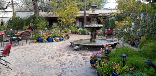A charming garden courtyard with a fountain, colorful flowers, and seating areas surrounded by greenery.