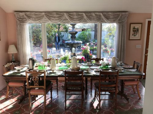 A beautifully set dining table with green accents, overlooking a garden with a fountain and blooming flowers.