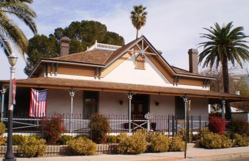 A charming house with a brown roof, palm trees, and an American flag, surrounded by a decorative fence and colorful plants.