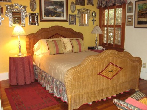 Cozy bedroom featuring a wicker bed, decorative mirrors, and warm lighting, with a patterned rug and bedside table.