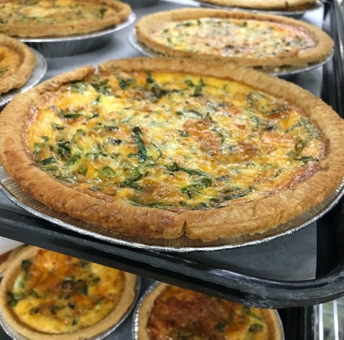 Freshly baked quiches with golden crusts and green herbs, displayed on trays.
