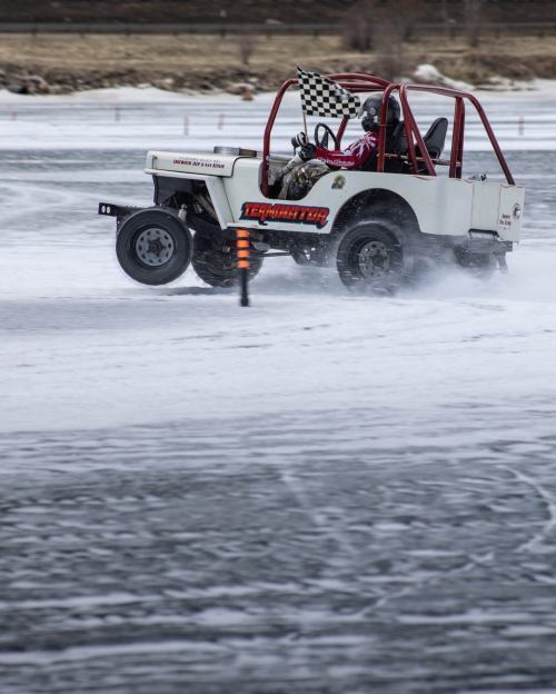 A modified vehicle races on icy terrain, with a driver waving a checkered flag amidst a snowy landscape.