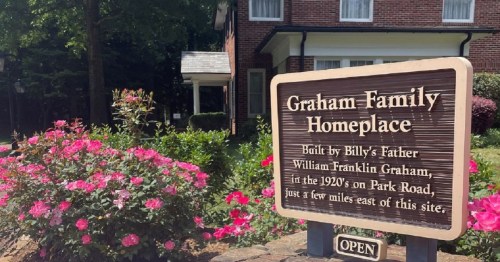 Sign for the Graham Family Homeplace, surrounded by flowers, with a brick house in the background.