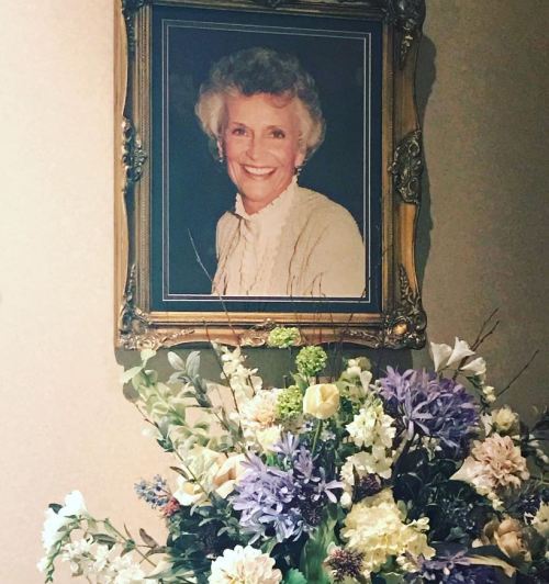 A framed portrait of a smiling woman hangs above a colorful floral arrangement.