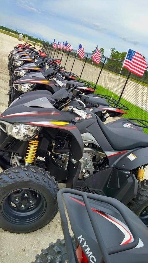 A row of black ATVs lined up with American flags in the background on a cloudy day.