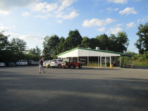 A small restaurant with a green roof, surrounded by parked cars and trees, under a partly cloudy sky.
