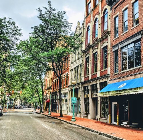 A quiet street lined with historic brick buildings and trees, featuring shops and a sign for "Capitol."