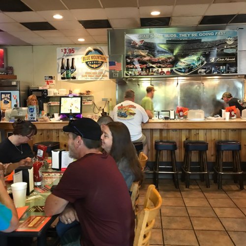 A busy diner with patrons at tables, a counter with staff, and a menu board in a casual setting.