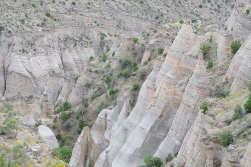 A rugged landscape featuring steep, layered rock formations and sparse vegetation in a canyon setting.