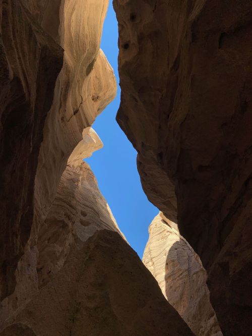 A narrow canyon with towering rock walls, framed by a bright blue sky above.
