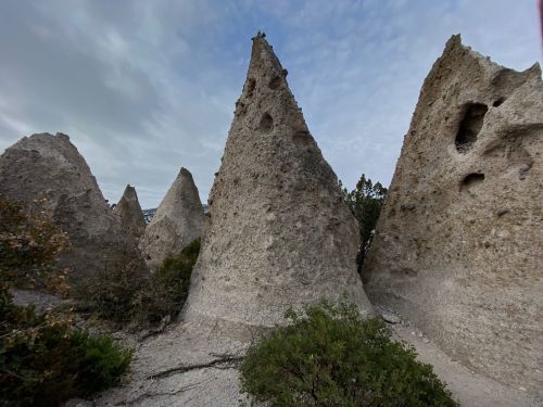 Unique rock formations resembling conical peaks, surrounded by sparse vegetation under a cloudy sky.