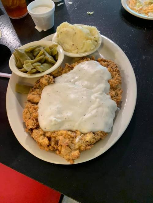 A plate of fried chicken smothered in white gravy, served with green beans and mashed potatoes on the side.