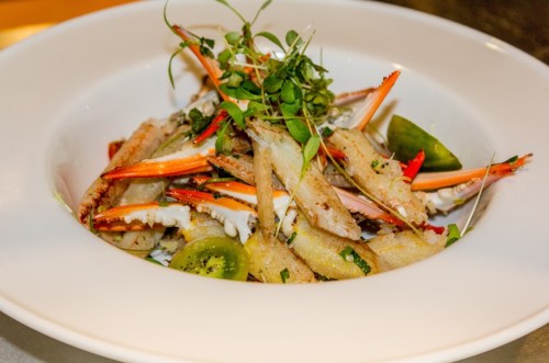 A gourmet dish featuring crab, herbs, and garnishes served in a white bowl.