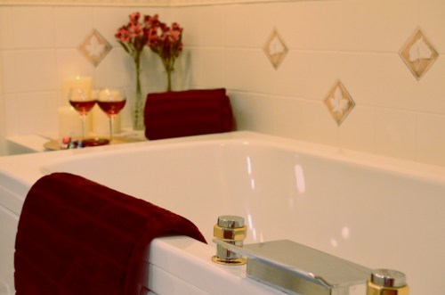 A luxurious bathroom with a white bathtub, red towels, candles, and decorative flowers.