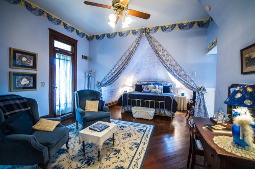 Cozy bedroom with blue decor, a canopy bed, two armchairs, and a small table, featuring elegant curtains and wooden accents.