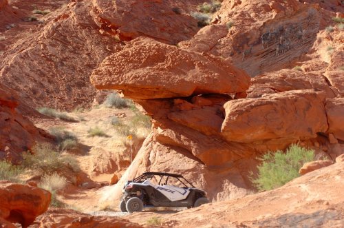 A rugged off-road vehicle navigating a rocky desert landscape with large red rock formations.