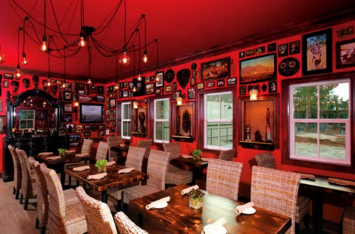 Cozy restaurant interior with red walls, wooden tables, woven chairs, and an array of framed photos and artwork.