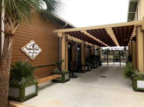 Entrance to a building with a sign reading "Seagull Club," featuring palm trees and a covered walkway.