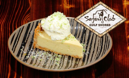 A slice of key lime pie topped with whipped cream, served on a decorative plate with a logo for Safari Club Gulf Shores.