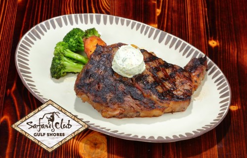Grilled steak with herb butter, served with broccoli on a white plate, set against a wooden table.