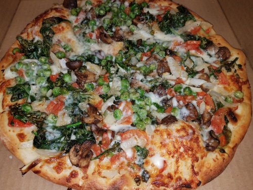 A freshly baked pizza topped with spinach, mushrooms, tomatoes, peas, and melted cheese on a golden crust.