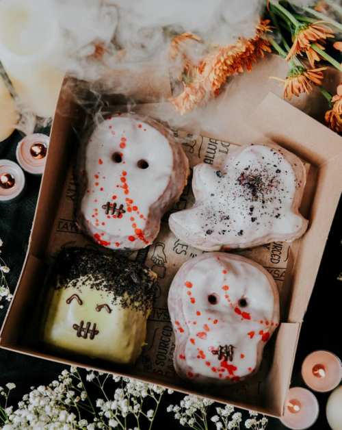 A box of Halloween-themed donuts shaped like ghosts and a monster, decorated with icing and sprinkles.
