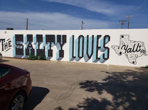 Mural featuring bold text "The Salty Loves Y'all" with a Texas outline, set against a blue sky.