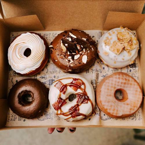 A box of six assorted donuts, featuring chocolate, caramel, and cream toppings, with various decorative designs.