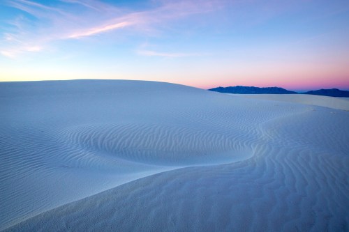 A serene desert landscape with white sand dunes under a pastel sky at dusk.
