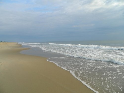 A serene beach scene with gentle waves lapping at the sandy shore under a cloudy sky.