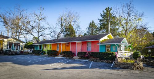 Colorful motel with vibrant doors, surrounded by trees and a parking area, set against a clear blue sky.