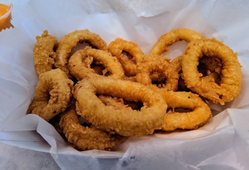 A serving of golden-brown fried onion rings piled on white paper.