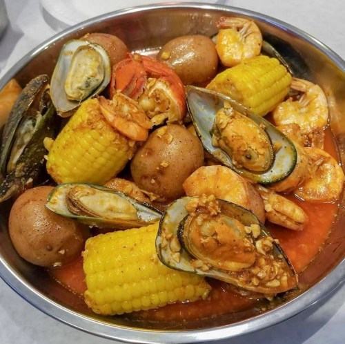 A bowl of seafood featuring shrimp, mussels, corn, and potatoes in a spicy sauce.