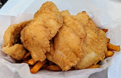 A serving of crispy fried fish fillets on a bed of golden French fries.