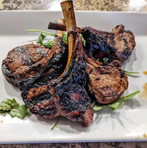 Grilled lamb chops arranged on a plate with fresh greens, showcasing a charred, flavorful exterior.