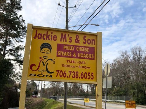 Sign for Jackie M's & Son, advertising Philly cheese steaks and hoagies, open Tuesday to Saturday, 11 AM to 8 PM.