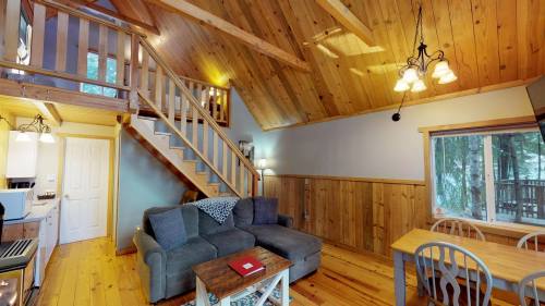 Cozy wooden cabin interior with a living area, staircase, and dining table, featuring natural light and rustic decor.