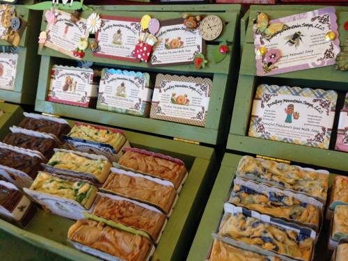 Colorful handmade soaps displayed on green shelves, with decorative labels and small embellishments.