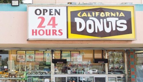 Sign for California Donuts, open 24 hours, with a display of various donuts visible in the shop window.
