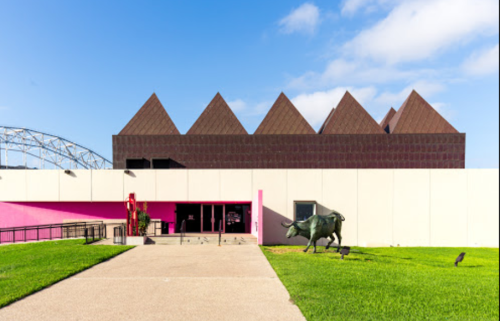 A modern building with pyramid-shaped roofs, pink accents, and a bull statue in front, set against a blue sky.
