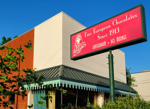 A building with a sign reading "Stan Fine European Chocolates Since 1913" in Amsterdam, Des Moines, against a clear blue sky.