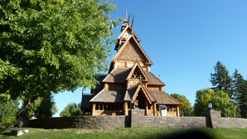 A wooden church with intricate architecture, surrounded by trees and a clear blue sky.