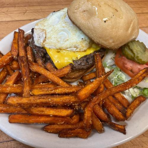 A juicy burger with cheese and a fried egg, served with crispy sweet potato fries, lettuce, tomato, and pickles.